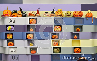 The wall with various halloween carved orange pumpkins crafted by children at the education school. Alphabet letters and Stock Photo