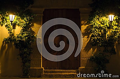 Wall with vintage massive wooden door and two lit street lamps Stock Photo