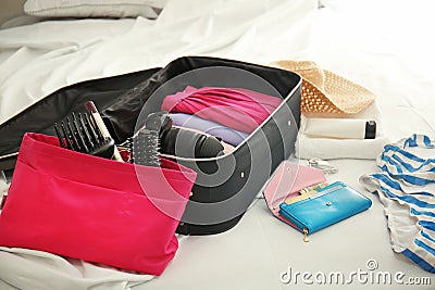 Wallet, hairbrushes and open suitcase with packed things on bed Stock Photo