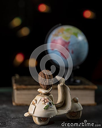 A walnut resting on a miniature scooter with a globe on a book in the background and bokeh of colored fairy lights Stock Photo
