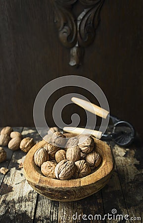 Walnuts with and without shell in a wooden bowl on a wooden rustic background with tongs for cracking nuts Stock Photo