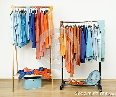 Wardrobe with complementary colors orange and blue clothes on hangers. Stock Photo