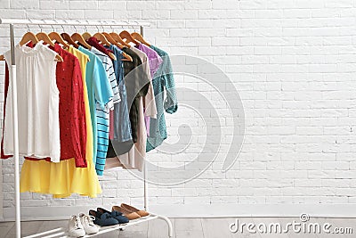 Wardrobe rack with stylish clothes and shoes near brick wall indoors. Stock Photo