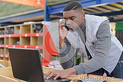 Warehouse manager using telephone and laptop in large warehouse Stock Photo