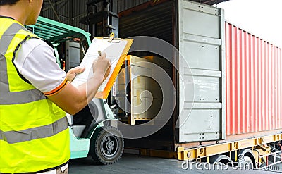 Warehouse worker holding clipboards control forklift loading shipment goods into container truck. Stock Photo