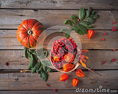 Warm autumn still life with pumpkin, rowan and physalis in a ceramic arrow in orange tones on wooden table, top view Stock Photo