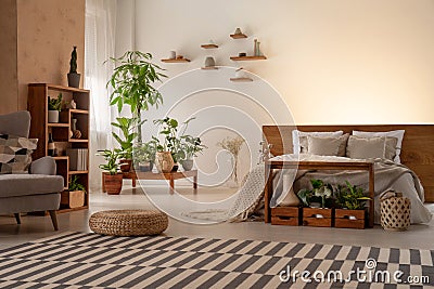 Warm bedroom interior with plants, shelves, striped rug, pouf, b Stock Photo