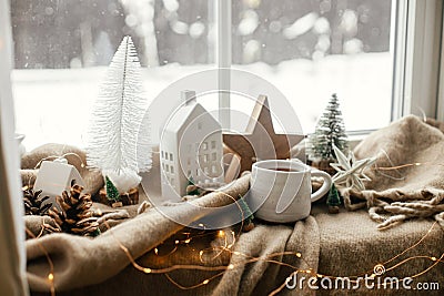 Warm cup of tea, christmas decor and lights on cozy blanket at window. Christmas Winter hygge Stock Photo