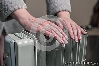 Warm hands over an oil-filled mobile heater. It`s cold at home, electricity is expensive Stock Photo