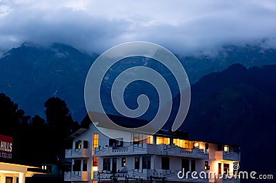 The warm lights from a building against the cool backdrop of fog covered mountains in the hill station of McLeodganj Editorial Stock Photo