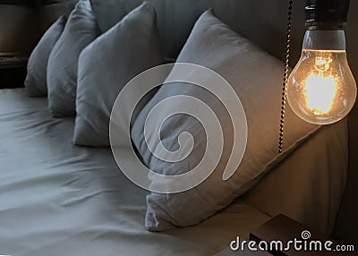 The warm orange glowing incandescent light bulb on the head of the white wooden bed. Loft Interior Design, comfortable and relax Stock Photo