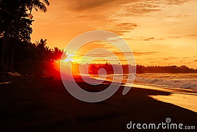 Warm sunset or sunrise with ocean waves and palms at black sand beach Stock Photo