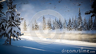 Warm, thermal mist rises from the river surrounded by snow and pine trees Stock Photo