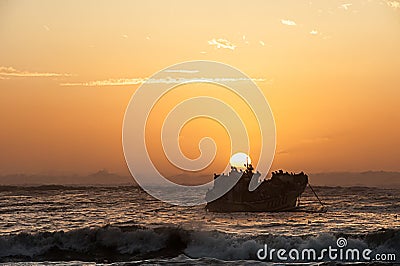 Warm toned image of a sunset with a ship wreck and a flock of sea birds silhouetted against the sunset Stock Photo