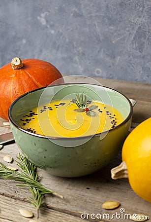 Warming autumn cream pumpkin soup in a green bowl. Pumpkins, rosemary twigs, pumpkin seeds on a wooden table Stock Photo