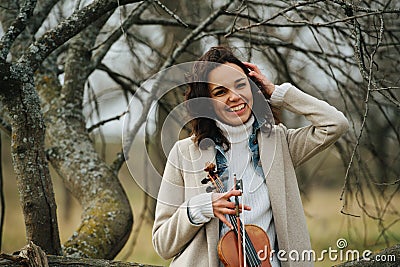 Warmly dressed woman with violin over leafless autumn lichen-covered trees Stock Photo
