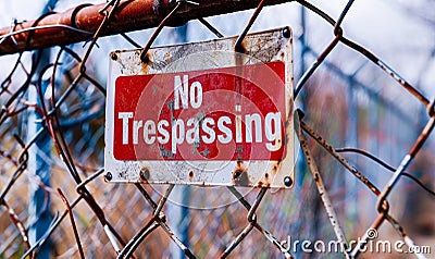 Warning sign No Trespassing mounted on a chain-link fence, with a weathered, bold red background, enforcing property boundaries Stock Photo