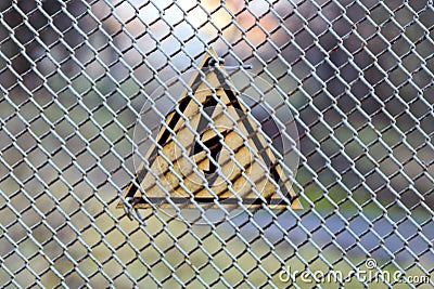 Warning triangular sign on a gray iron shallow grid of a fence Stock Photo