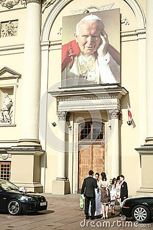 newly married young people standing in front of a church with a giant picture of John Paul II, Editorial Stock Photo