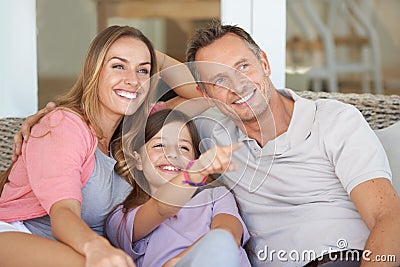 It was still their favourite movie. A young girl sitting on a couch with her parents and pointing to something. Stock Photo