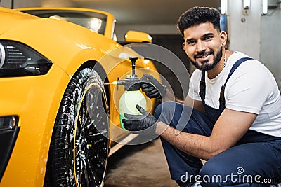 Indoor shot of male worker in overalls, washing the car wheels rims Stock Photo