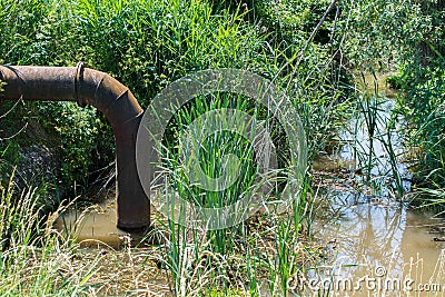 Wastewater polluting the small pond trough rusty iron pipe Stock Photo