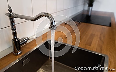 Water flowing out of a kitchen stainless steel tap into the sink. Water misuse in domestic duties and activities. Overusing Stock Photo