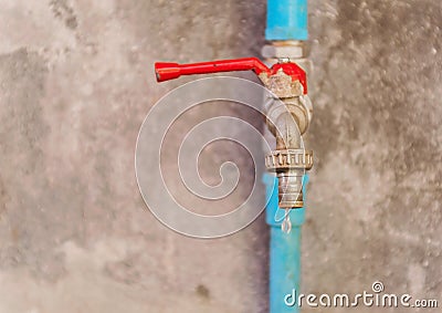 Wasting water, Water drop from old water tap on grunge wall back Stock Photo