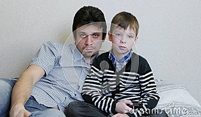 Watching TV lying on the couch. Bored boy and his dad are watching TV and switches the channels. Stock Photo