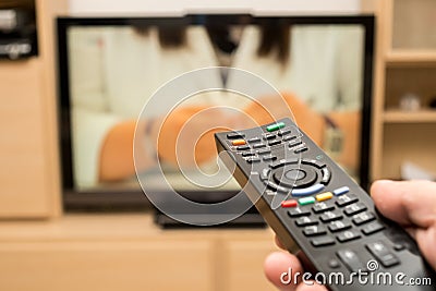 Watching TV and using black modern remote controller. Hand holding TV remote control with a television in the background Stock Photo