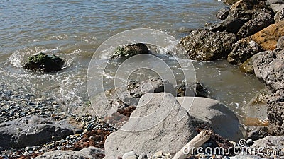 Water comes to rocky shore. Concept. Dirty water on rocky shore. Dirty sea water with small waves breaks on rocks. Rocky Stock Photo