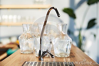 Water crane on the background of many glass large vases standing on a wooden countertop Stock Photo