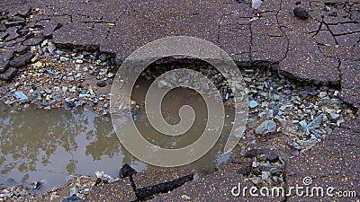 Water erosion of the road. Broken asphalt background. Danger hole, stone gray backdrop. Stock Photo