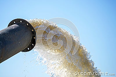 Water flows from a metal pipe against a blue cloudless sky. The concept of wastewater discharge Stock Photo