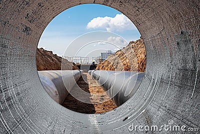 Water pipes for drinking water supply lie on the construction site. View from a large concrete pipe. Preparation for earthworks Stock Photo