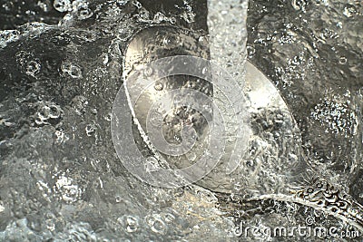 Water pours on the spoon in a strong stream and you can see the iridescent drops in the light. Closeup Stock Photo