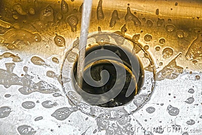 Water running into a garbage disposal of a stainless steel sink with gold toned blurred background and sharp silver foreground Stock Photo