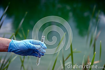 Water sample. A man`s hand in a blue glove holds a test tube with a water sample. Background Stock Photo