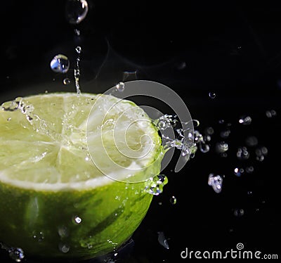 Water splashing over half a lime. Black background. Stock Photo
