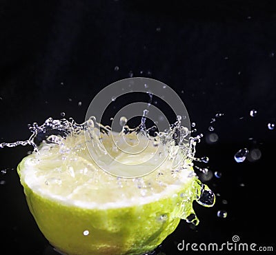 Water splashing over half a lime. Black background. Stock Photo