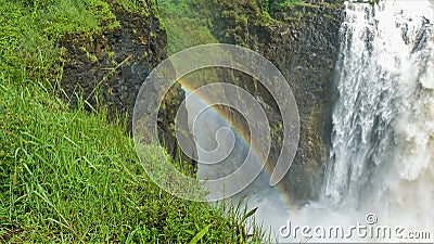 Water streams fall into the gorge. A rainbow formed between the stony slopes. Stock Photo