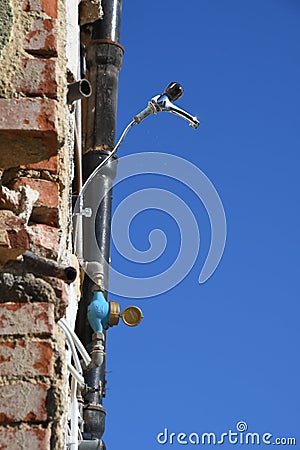 Single water tap reaching out of facade of ruined house Stock Photo