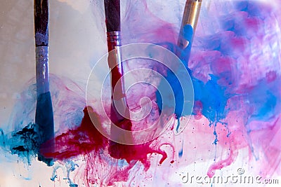 In the water are three paint brushes with blue and red paints Stock Photo