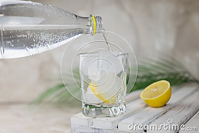 Water or tonic is poured from a bottle into a glass with ice Stock Photo