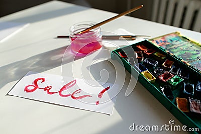 Watercolor inscription Sale on white sheet of paper, on table in Stock Photo