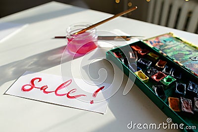 Watercolor inscription Sale on white sheet of paper, on table in Stock Photo