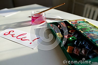 Watercolor inscription Sale on white sheet of paper, on table in Stock Photo