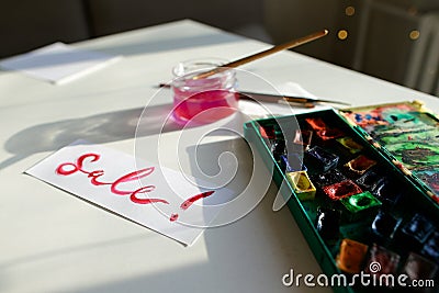 Watercolor inscription Sale on white sheet of paper, on table in Stock Photo