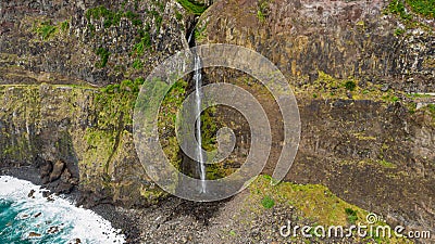Waterfall falling into ocean from volcanic cliffs. Stock Photo
