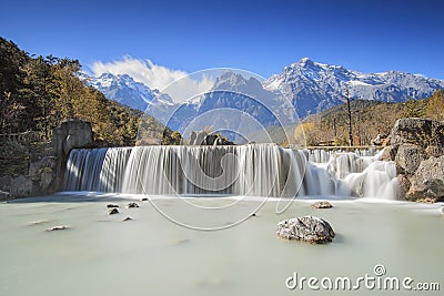 Waterfall on foreground and Jade Dragon Snow Mountain on background - Yunnan, China Stock Photo